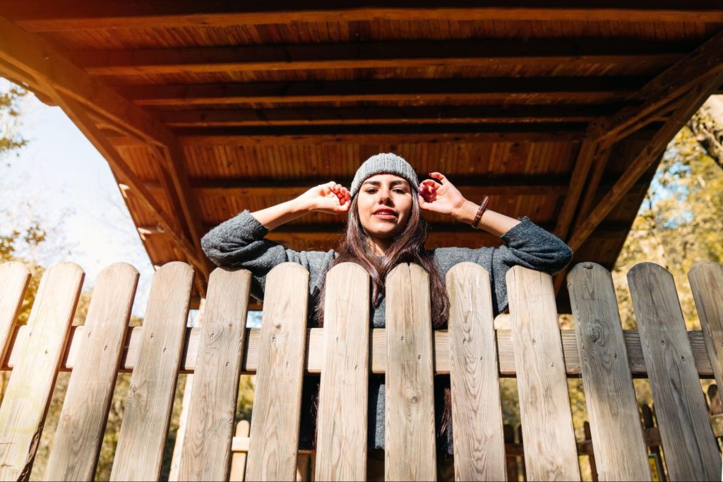 Woman in a beanie leaning on a fence.