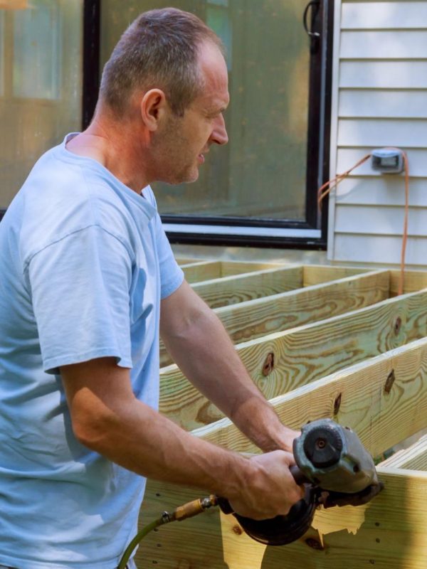 An adult man installing a wooden deck patio.