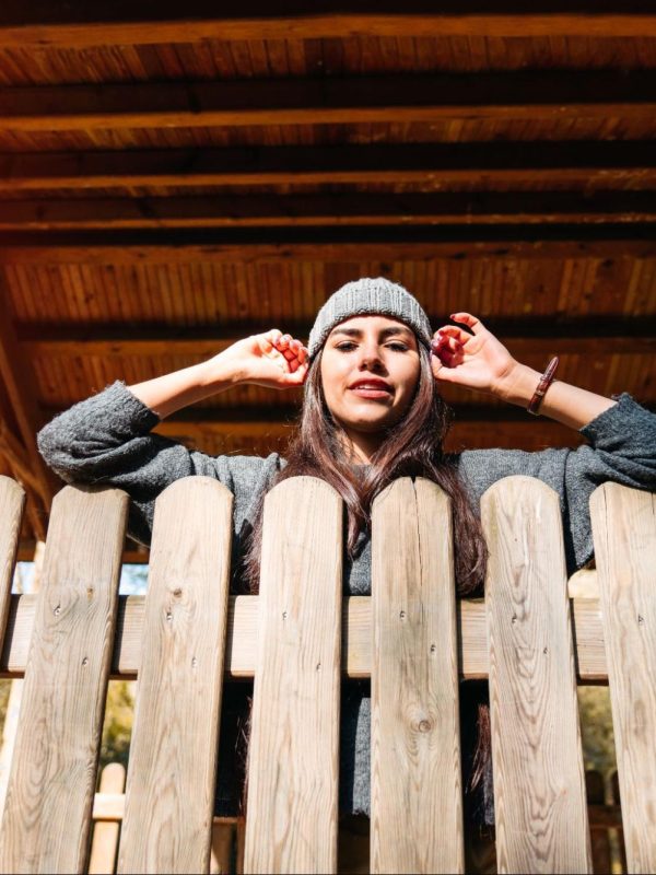 Woman in a beanie leaning on a fence.