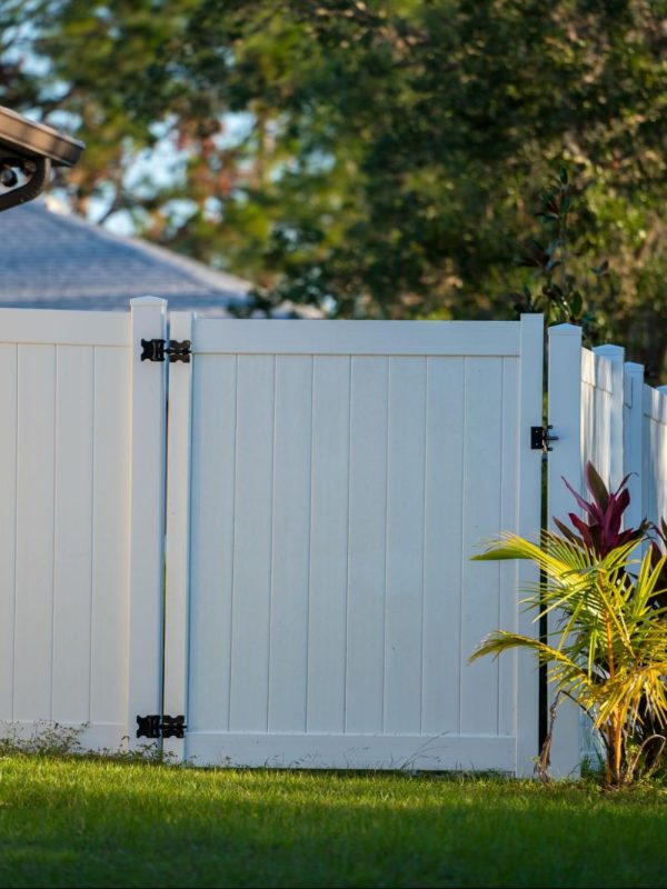 Elegant white vinyl picket fence on a lush green lawn, enclosing the property with well-manicured landscaping in front.