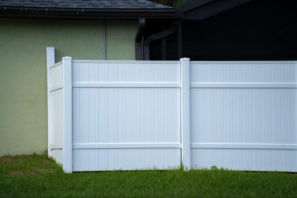 White vinyl picket fence at the back of a residential house.