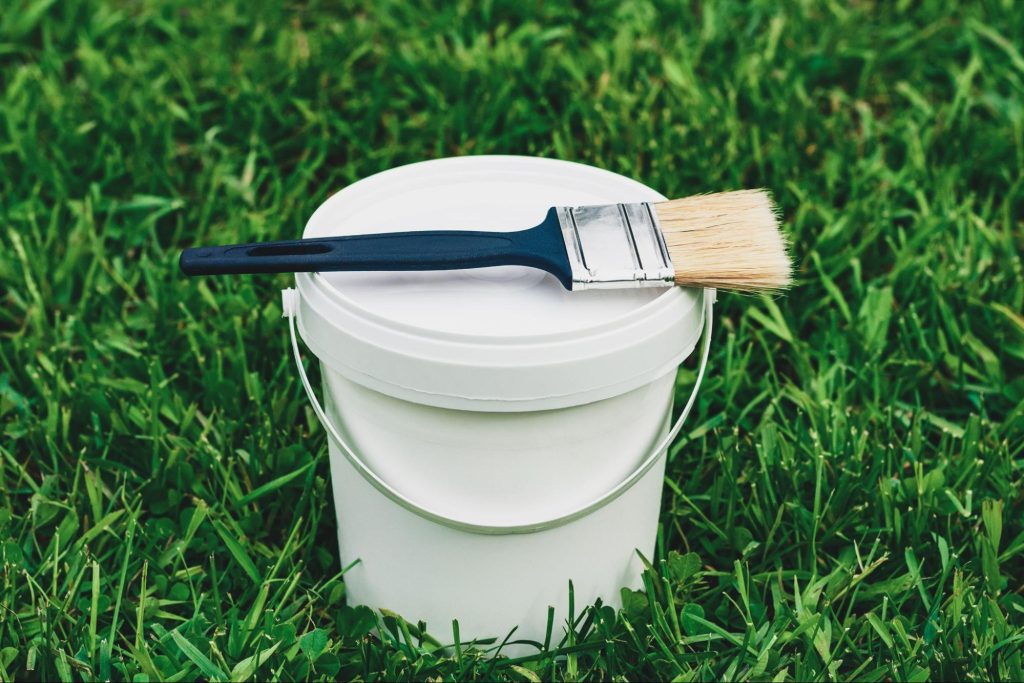 Paint bucket and a brush on a lawn.