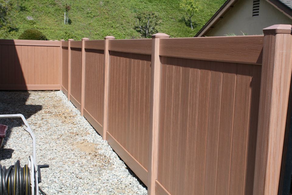 150165_413825608657573_494124519_n A row of vertical wooden fence panels with decorative post caps on a bed of gravel with a house and greenery in the background. A hose reel is partially visible on the left side.