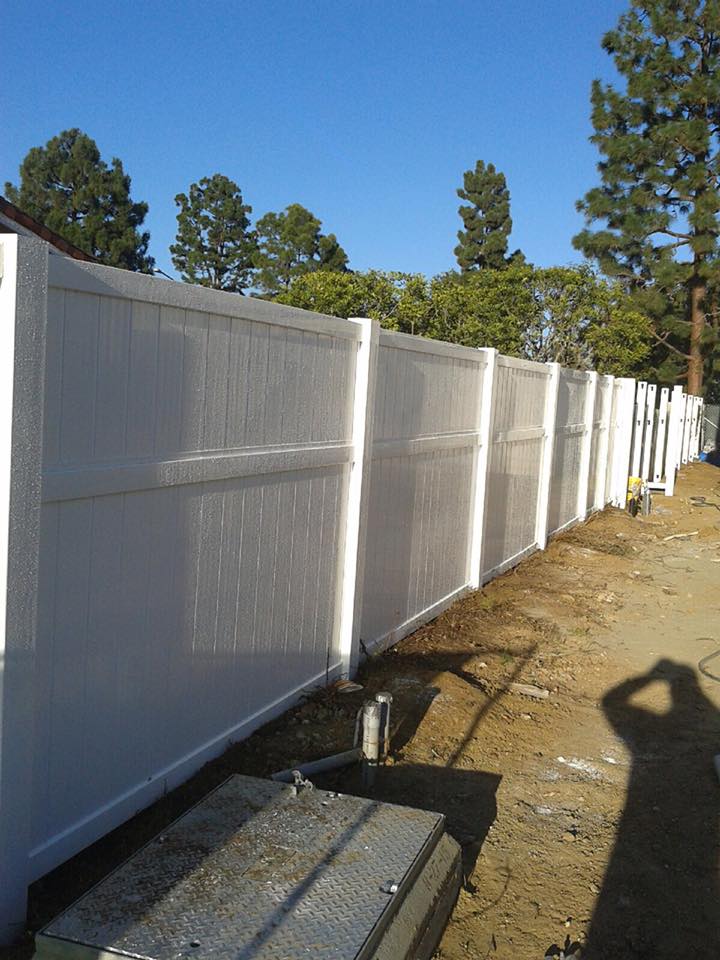 image 2 A white vinyl fence installed along a dirt path with trees and a blue sky in the background.