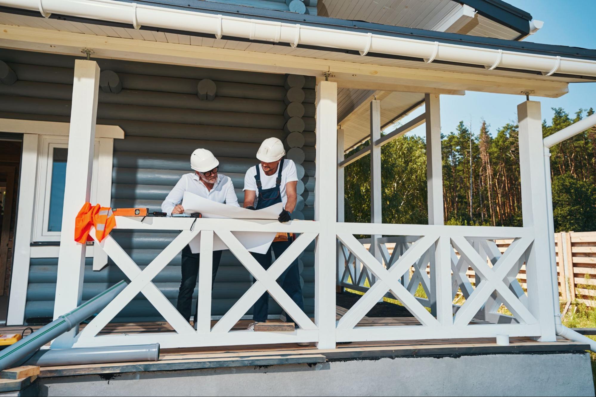 Two male workers wearing safety caps are leaning over the paper layout during the building process.