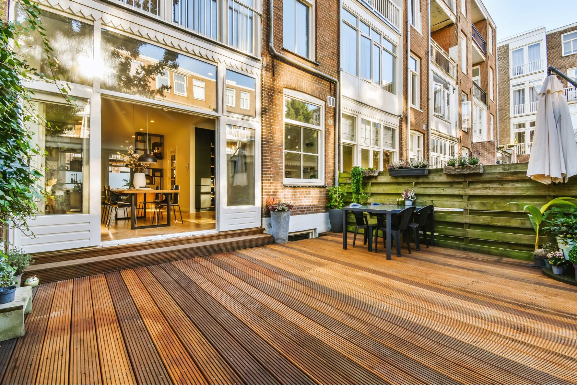 A stylish deck with a few potted plants, a white table set indoors, and a black table set outdoors.
