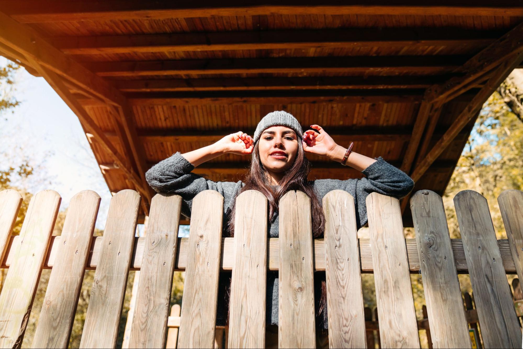 Woman in a beanie leaning on a fence.