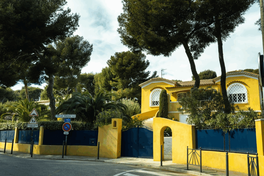Yellow villa with a blue metal gated fence supported by yellow concrete pillars, combining structure and vibrant design.