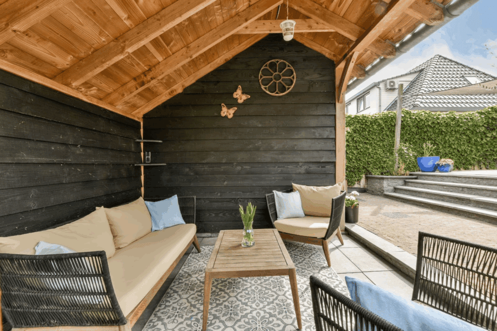 Accessible covered patio with wooden roof structure, cushioned outdoor couches, and a central table arranged for comfort and conversation.