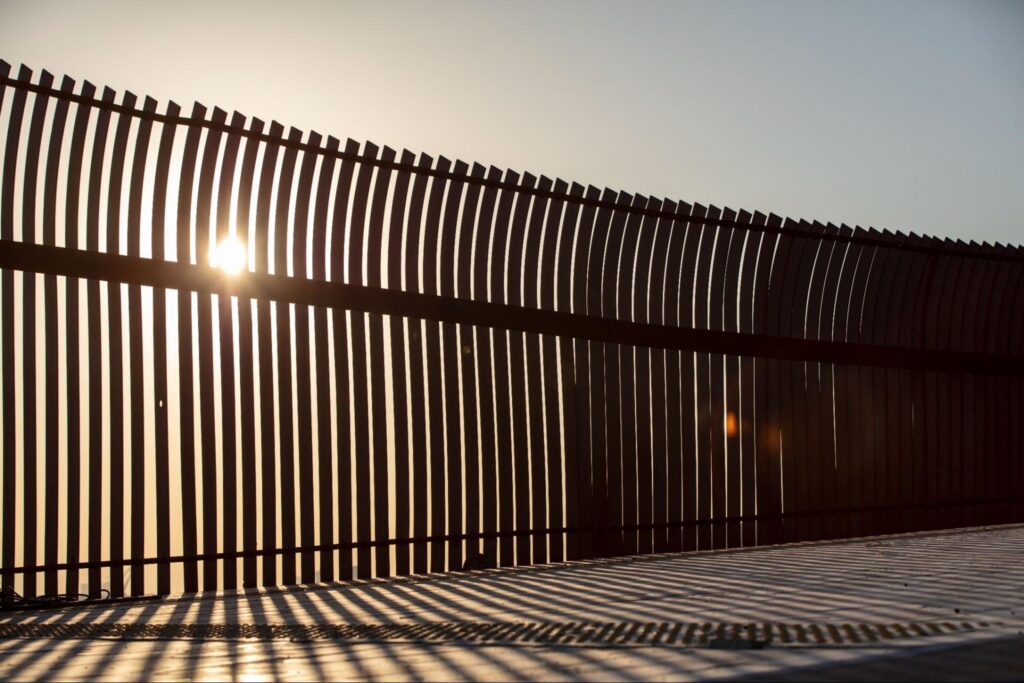 Silhouette of an aluminum fence along a beach shoreline at sunset.