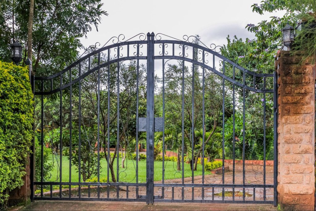 A black steel fencing gate at the entrance of a garden-fronted property.