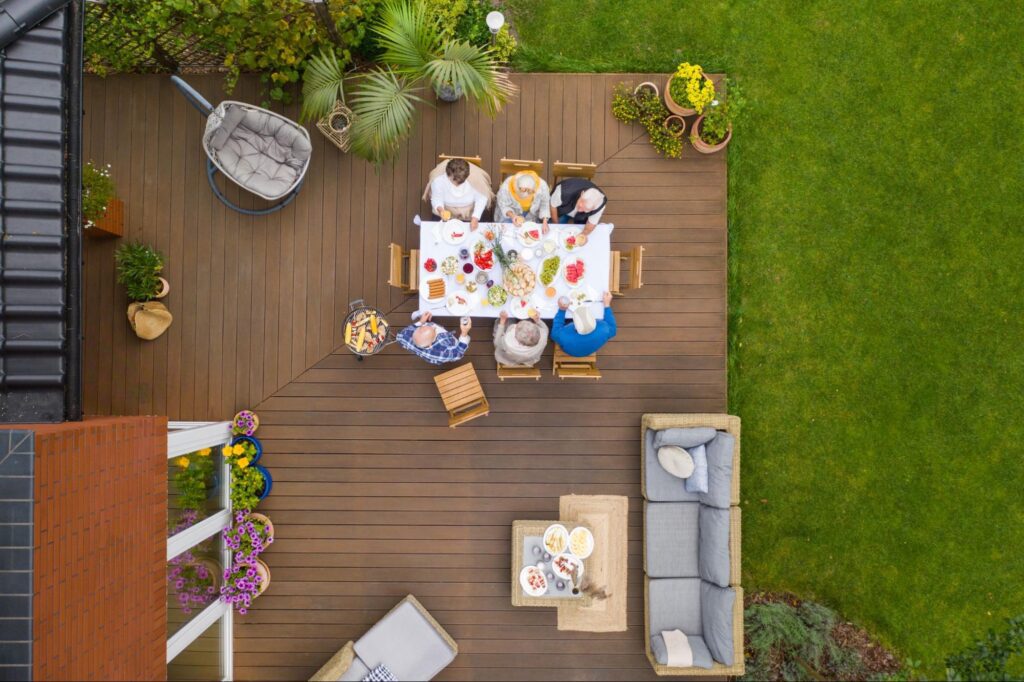 Top view of a backyard deck featuring people gathered around a dining table under an open sky.