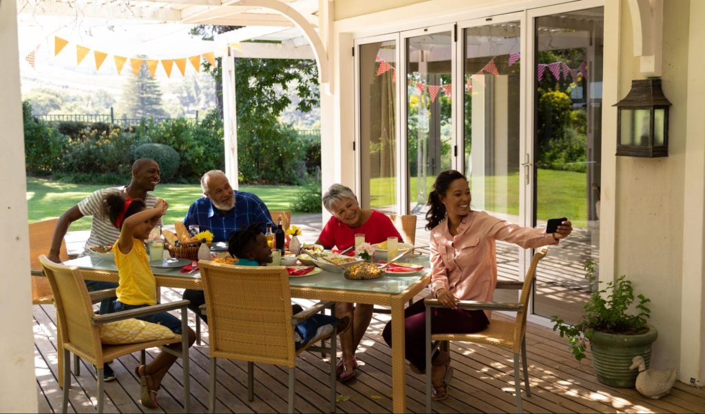 Family sitting outdoors taking a photo at a table with a vinyl patio cover overhead.