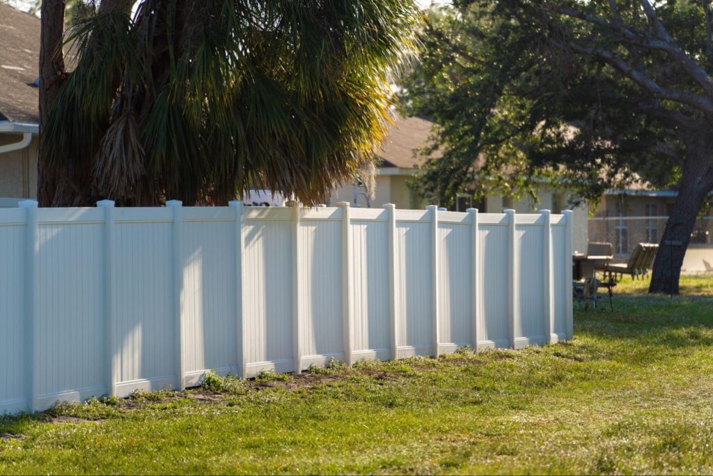 A side view of a white vinyl fence outside of a home.